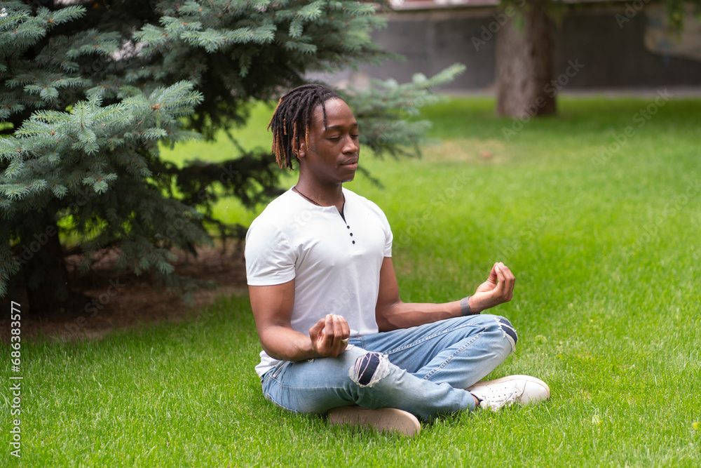 a stylish man meditating and doing yoga on the grass in the park