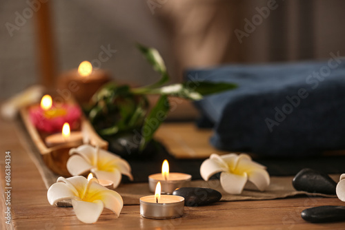 Burning candles with plumeria flowers on table in dark spa salon, closeup