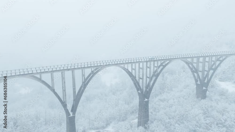 old arch bridge in winter season, Tara bridge in Montenegro, snow covered landscape. Aerial view during snowfall