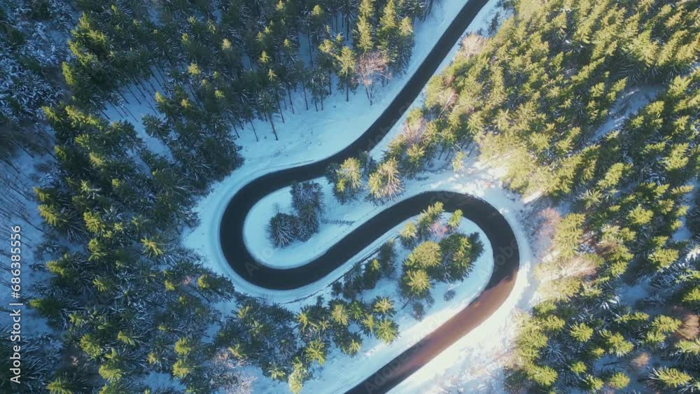 Twisted road in winter forest. Asphalt road serpentine and snowy landcape around. Aerial 4K footage from drone flight