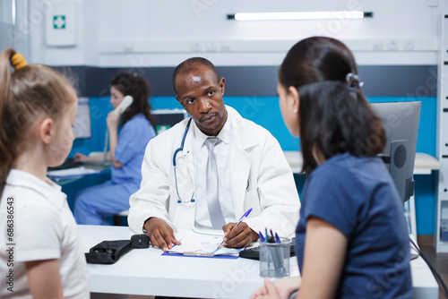 In hospital office, doctor consults with a caucasian woman and her daughter, discussing a medical condition, and providing advice and treatment options. Professional and caring atmosphere.