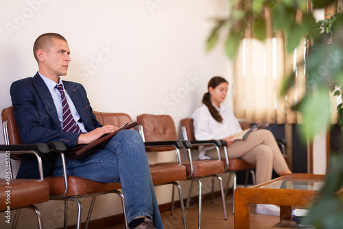 Focused young male is sitting in the lobby of a large company waiting for his turn to see a specialist
