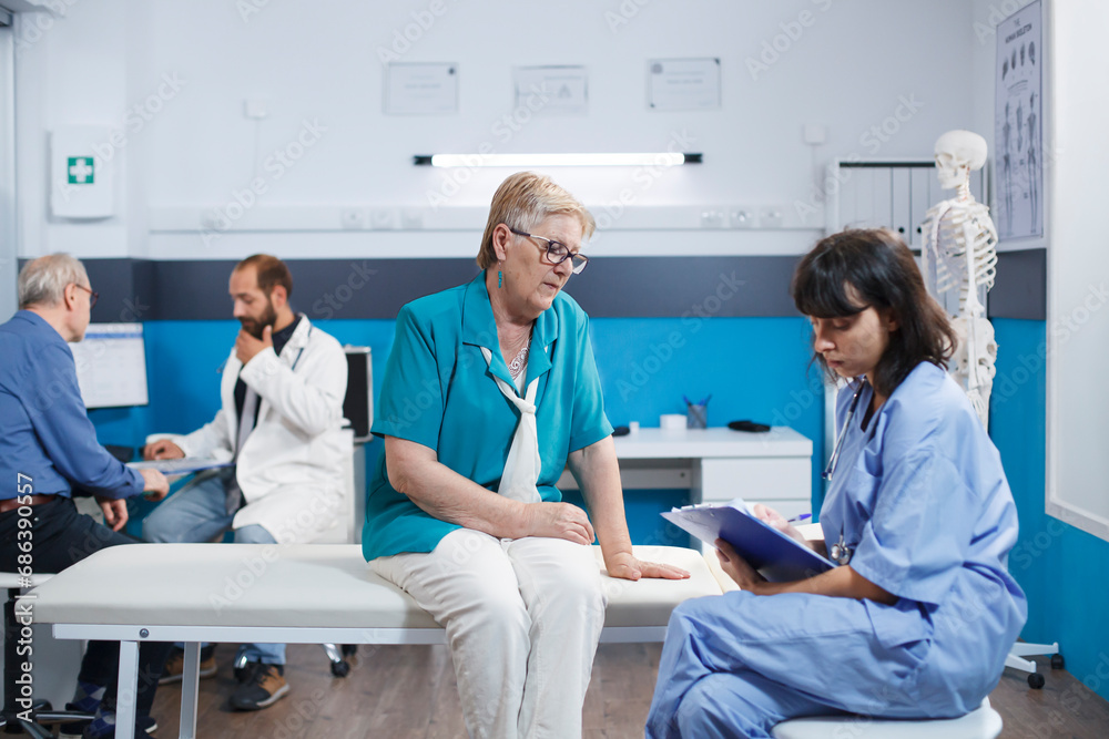Obraz premium Elderly woman receives checkup from healthcare practitioner in blue scrubs. Retired senior patients in hospital room getting medical examinations from professional physiotherapists.