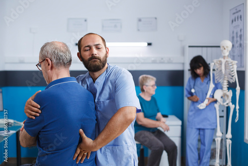 Orthopedic physician stretches spine and shoulder of senior patient with injury for physiotherapy. Medical practitioner giving help to retired old man with back pain for physical recovery.