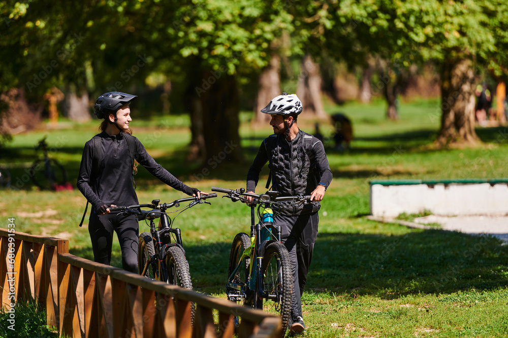 A blissful couple, adorned in professional cycling gear, enjoys a romantic bicycle ride through a park, surrounded by modern natural attractions, radiating love and happiness A blissful couple, adorned in professional cycling gear, enjoys a romantic bicycle ride through a park, surrounded by modern natural attractions, radiating love and happiness