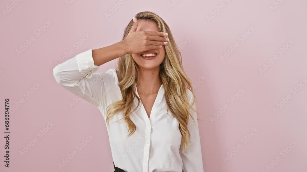 Young blonde woman hiding sparkling laughter over isolated pink background! wearing shirt, standing, covering eyes surprise-blind, hand on face, simply irresistible. Young blonde woman hiding sparkling laughter over isolated pink background! wearing shirt, standing, covering eyes surprise-blind, hand on face, simply irresistible.