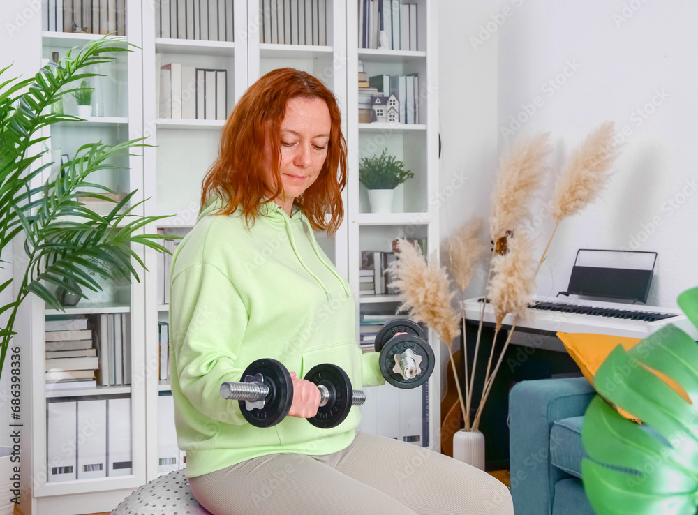 woman doing sports exercises with fitness ball and dumbbells at home