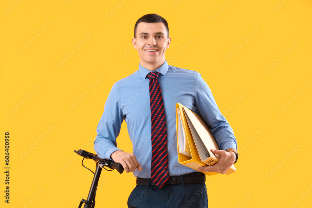 Young businessman with folders and electric scooter on yellow background Young businessman with folders and electric scooter on yellow background