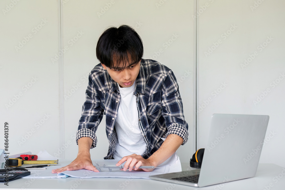 Young Asian engineer drawing construction project plans on plan paper on table in office Young Asian engineer drawing construction project plans on plan paper on table in office