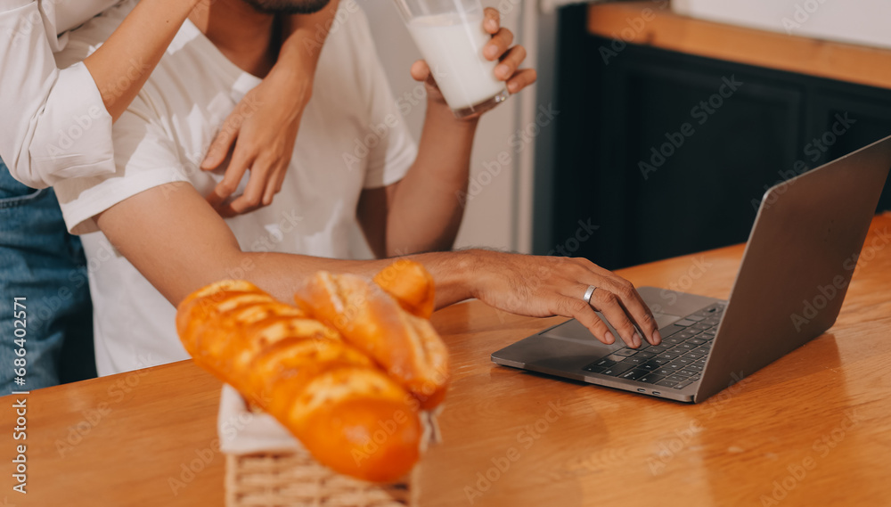 Handsome man sitting near his wife at kitchen. Family couple see social media, surf the web while sitting at kitchen table with generic laptop. Couple working with laptop at home