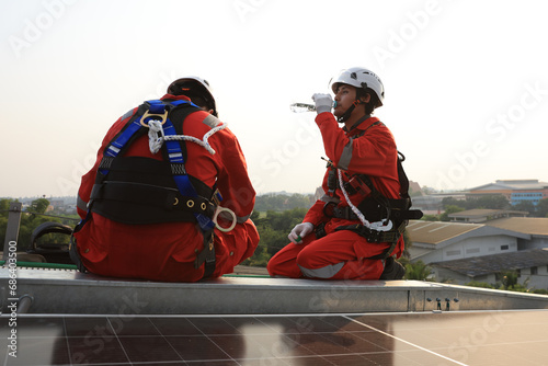 Fototapeta Naklejka Na Ścianę i Meble -  Two male Solar engineers with Red Safety Hazard dress  and wearing safety hardness resting during break time on working 