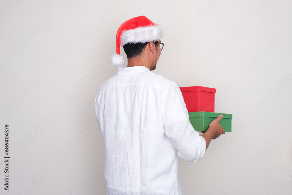 Back view of a man wearing christmas hat holding gift boxes