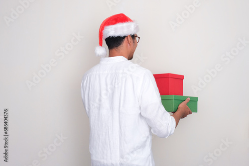 Back view of a man wearing christmas hat holding gift boxes photo