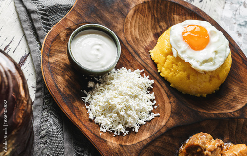 Delicious polenta with fried eggs, cheese and sour cream on wooden board over rustic background. Traditional romanian healthy food, top view photo