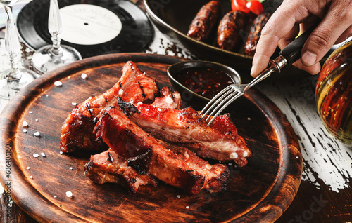 Hands cut barbecue pork spare ribs with hot honey chilli marinade on wooden cutting board with sauce on rustic background. Close up photo