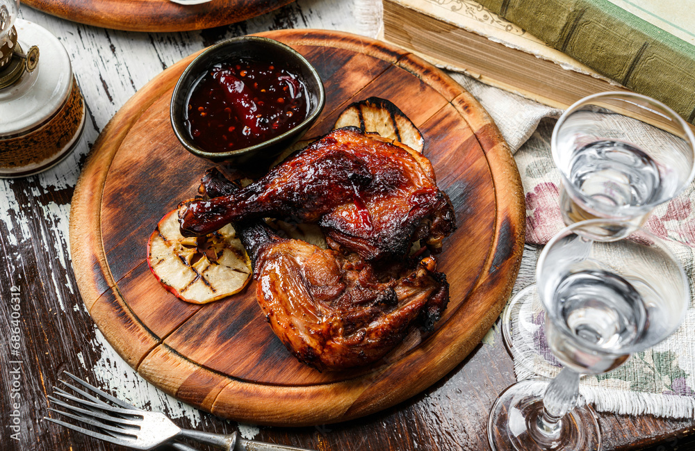 Grilled duck legs and bbq chicken meat with sauce, apples on wooden background with glasses of vodka. Holiday food, top view Grilled duck legs and bbq chicken meat with sauce, apples on wooden background with glasses of vodka. Holiday food, top view