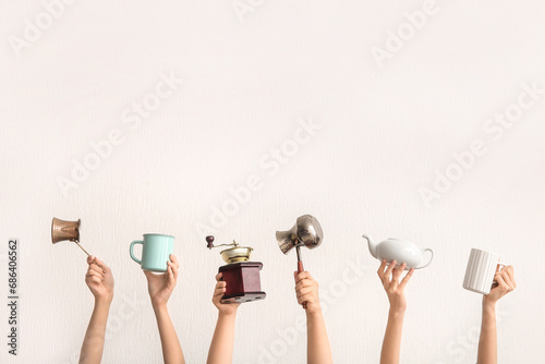 Female hands with coffee grinder, jezve, teapot and cups on light background