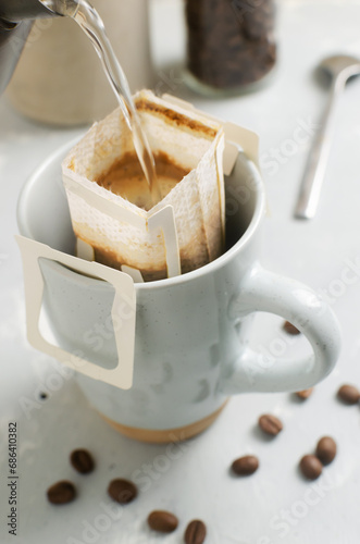 Fototapeta Naklejka Na Ścianę i Meble -  The process of brewing a bag Drip coffee into a cup on a gray background. A quick way to prepare a tasty and aromatic drink. Vertical orientation. Selective focus
