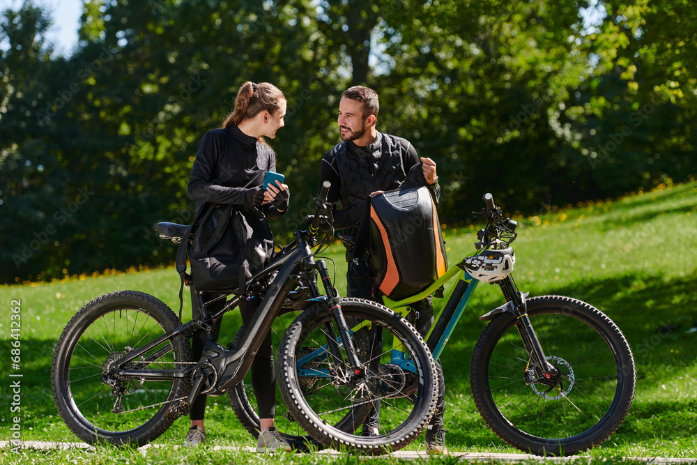 Fototapeta premium A sweet couple, equipped with bicycles and engrossed in coordinating their journey, checks their GPS mobile and watches while planning scenic routes in the park, seamlessly blending technology and