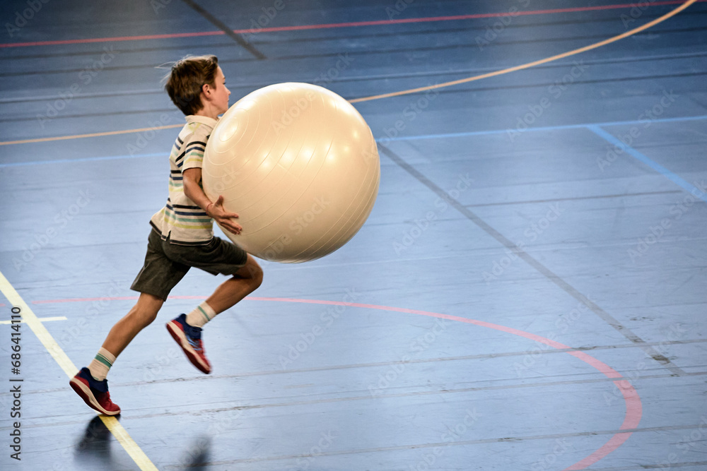 Énergie Sportive, jeune handballeur dribblant avec une grosse balle en plein élan - obrazy, fototapety, plakaty 