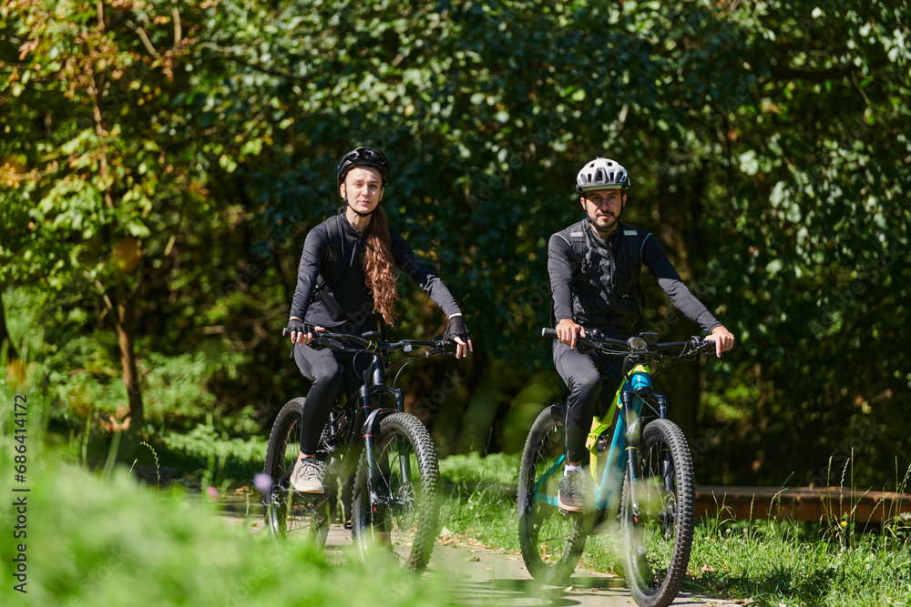A blissful couple, adorned in professional cycling gear, enjoys a romantic bicycle ride through a park, surrounded by modern natural attractions, radiating love and happiness A blissful couple, adorned in professional cycling gear, enjoys a romantic bicycle ride through a park, surrounded by modern natural attractions, radiating love and happiness