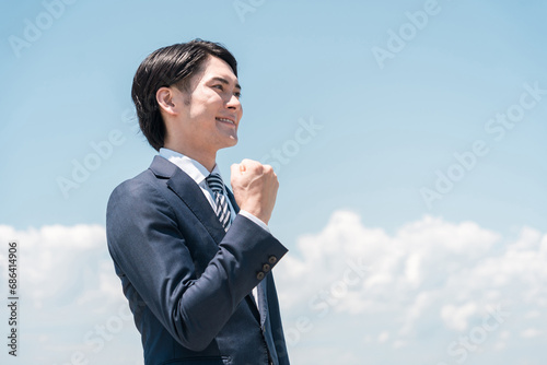青空の中ガッツポーズするビジネスマン・サラリーマン・スーツ姿の男性 