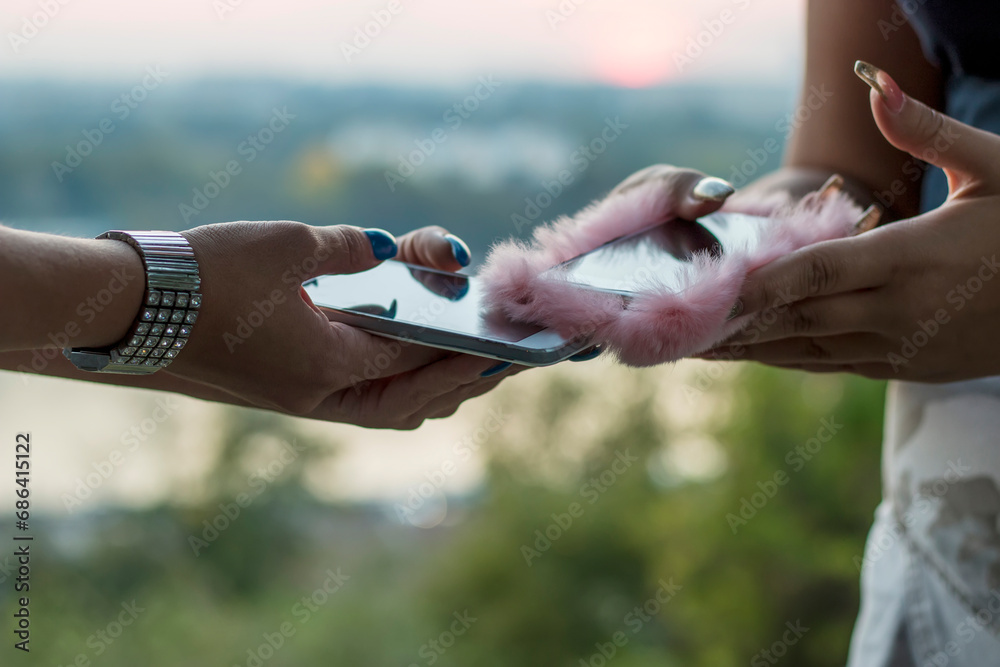 Close up view of two female hands using smartphone near the river during sunset Close up view of two female hands using smartphone near the river during sunset