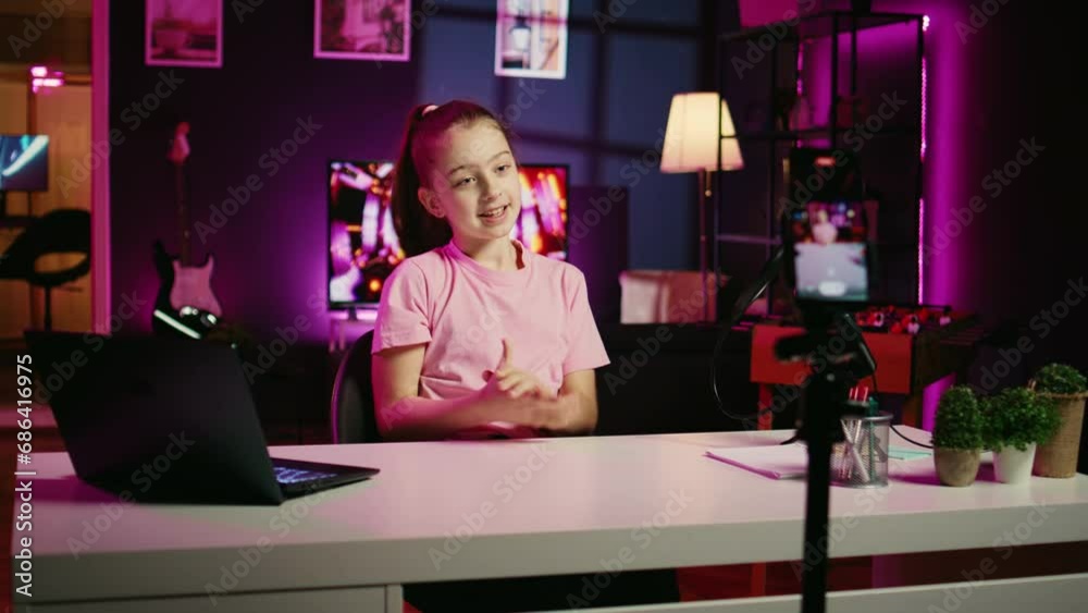 Zoom in shot of kid talking about school with children audience, filming content for social media with cellphone attached to tripod. Young girl recording video for internet channel with mobile phone Zoom in shot of kid talking about school with children audience, filming content for social media with cellphone attached to tripod. Young girl recording video for internet channel with mobile phone
