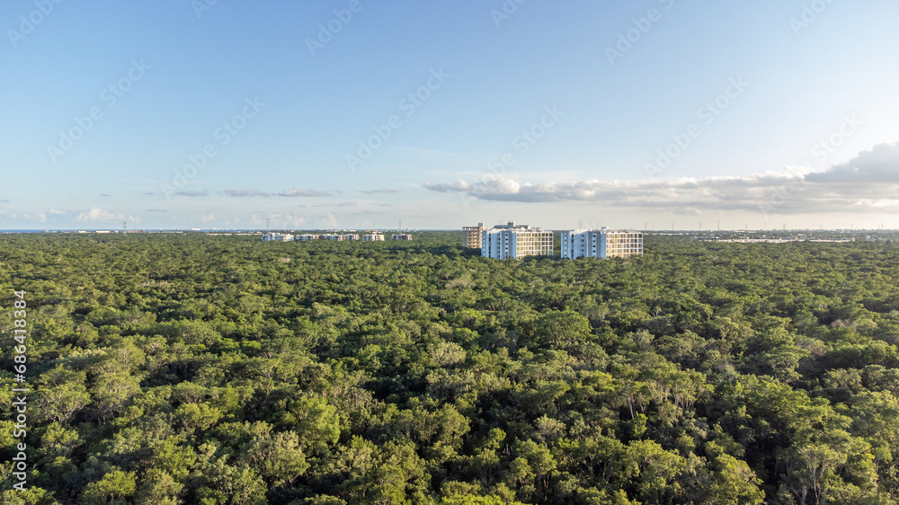 Aerial drone view of apartment surrounded by green tropical jungle in Tulum during golden hour with beautiful blue sky and few clouds