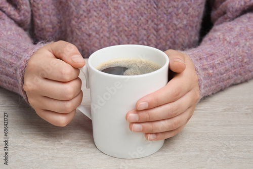 Woman holding white mug with coffee at wooden table, closeup