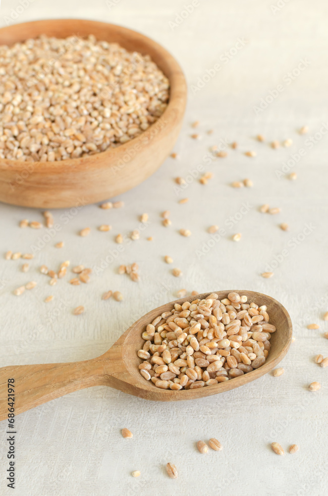 Wheat groats in a wooden spoon and a bowl on a light background. Rustic style. Concept of healthy food. Vertical orientation. Selective focus Wheat groats in a wooden spoon and a bowl on a light background. Rustic style. Concept of healthy food. Vertical orientation. Selective focus