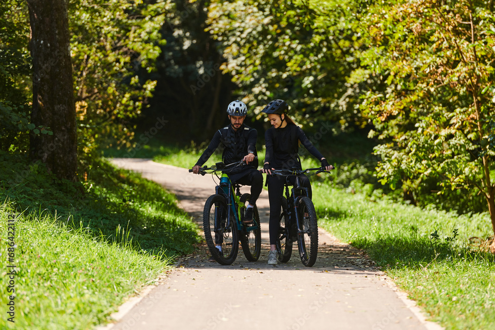 Naklejka premium A blissful couple, adorned in professional cycling gear, enjoys a romantic bicycle ride through a park, surrounded by modern natural attractions, radiating love and happiness