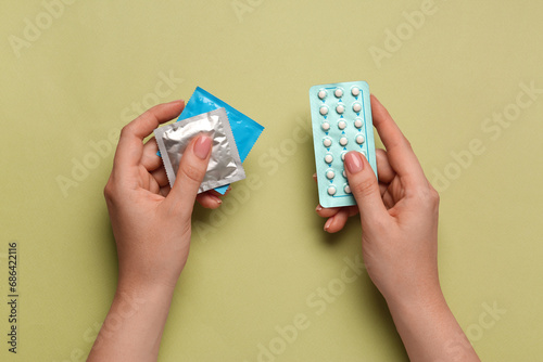 Woman with condoms and contraceptive pills on olive background, top view. Choosing birth control method photo
