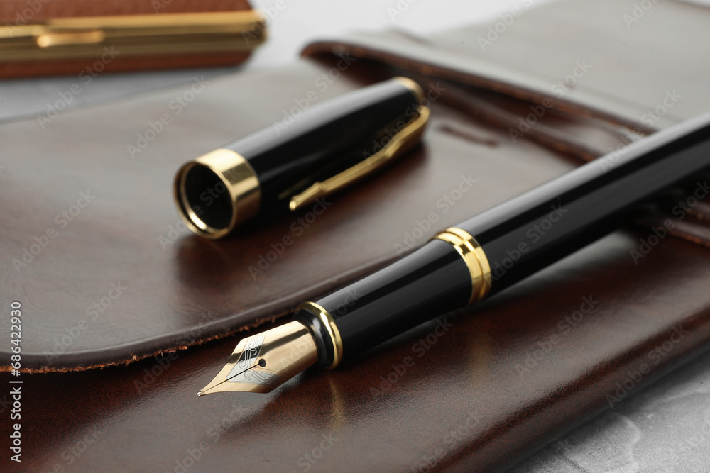 Stylish fountain pen, cap and leather notebook on light grey table, closeup Stylish fountain pen, cap and leather notebook on light grey table, closeup