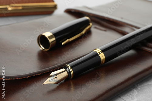 Stylish fountain pen, cap and leather notebook on light grey table, closeup