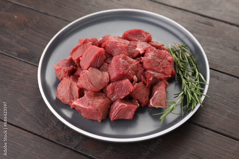 Pieces of raw beef meat with rosemary on wooden table Pieces of raw beef meat with rosemary on wooden table
