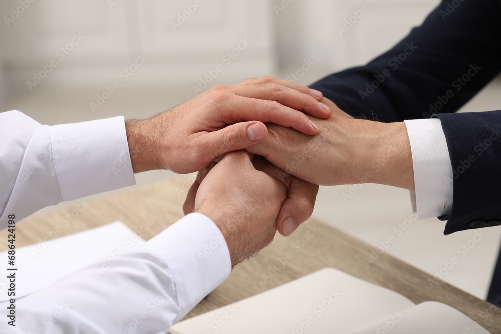 Trust and deal. Men joining hands at table indoors, closeup Trust and deal. Men joining hands at table indoors, closeup