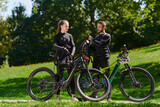 A sweet couple, equipped with bicycles and engrossed in coordinating their journey, checks their GPS mobile and watches while planning scenic routes in the park, seamlessly blending technology and