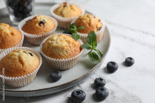 Delicious sweet muffins with blueberries and mint on white marble table, closeup. Space for text