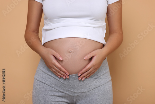 Pregnant woman in white T-shirt on beige background, closeup