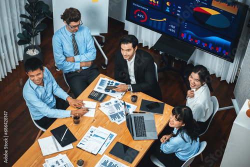 Wide top view of diverse group of business analyst team analyzing financial data report paper on meeting table. Chart and graph dashboard by business intelligence analysis. Meticulous