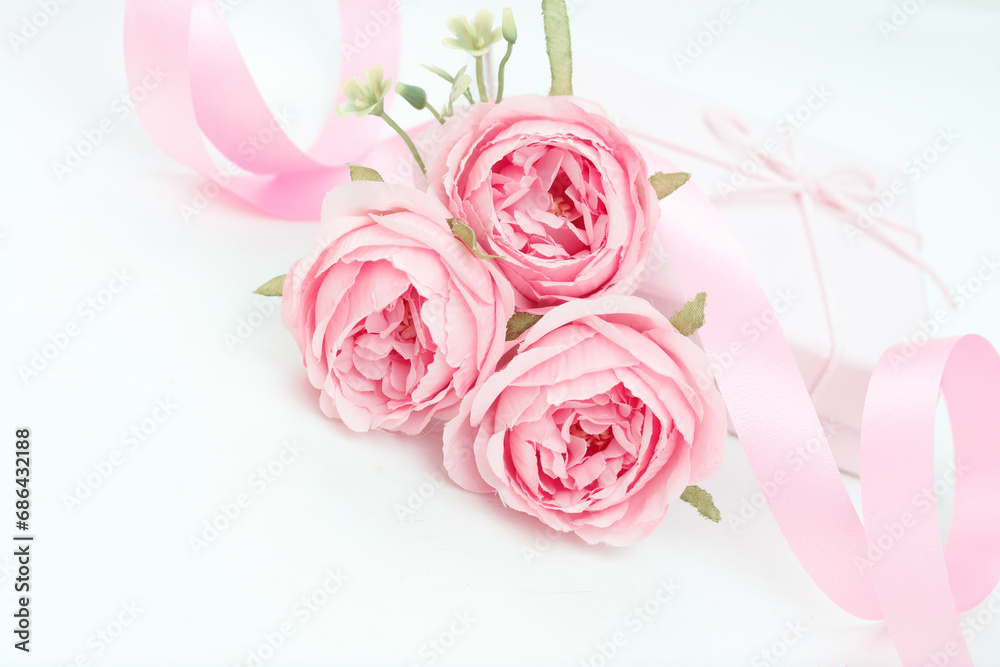 Three pink roses with ribbon and giftbox on the white table
