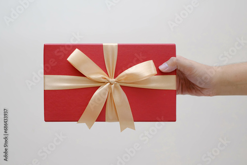 Fototapeta Naklejka Na Ścianę i Meble -  Male hands holding a small red gift box wrapped with gold ribbon. Isolated white background. Selective focus. Christmas Concept.