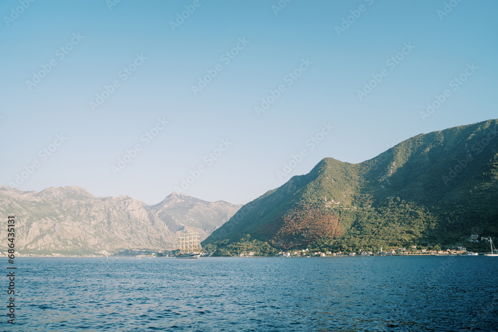 Large ship sails on the sea against the backdrop of green mountains