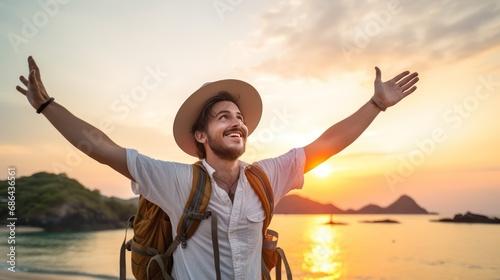 A Happy male traveler in hat and backpack raising arms on beach at sunset Delightful male traveler enjoying quiet time, travel and mental health. photo