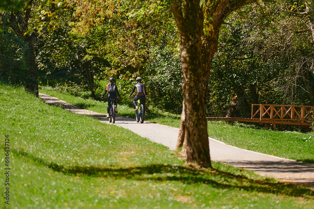 A blissful couple, adorned in professional cycling gear, enjoys a romantic bicycle ride through a park, surrounded by modern natural attractions, radiating love and happiness A blissful couple, adorned in professional cycling gear, enjoys a romantic bicycle ride through a park, surrounded by modern natural attractions, radiating love and happiness