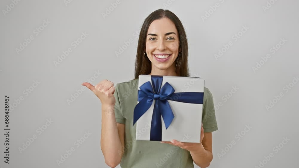 Joyful young hispanic woman confidently showing off her birthday present, thumb pointing good vibes to the side, isolated on a white cutout background.