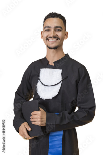Jovem pardo de barbicha, sorridente, magro, com beca de formatura e segurando o chapéu de formatura ao seu lado. Pose confiante. Felicidade. photo