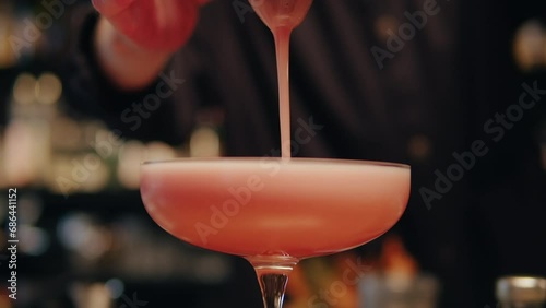 Bartender make a cocktail for guest in the bar. Pink foamy sour alcohol drink . Barman is doing drinks close-up. Modern bar with many varieties of cocktails and drinks. 