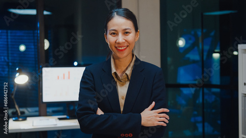 Portrait of successful executive businesswoman smart casual wear looking at camera and smiling, happy in modern night office workplace. Young Asia lady standing relax in contemporary meeting room.